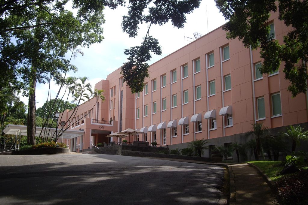 Prédio rosa do antigo Grande Hotel de Águas de São Pedro, entre palmeiras e árvores