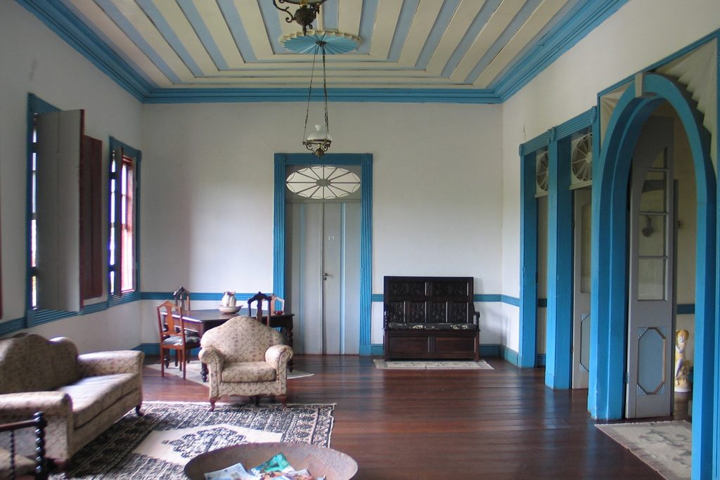 Sala ampla com forro pintado, portas e janelas de moldura azul, piso de madeira e móveis antigos, na Fazenda Boa Vista