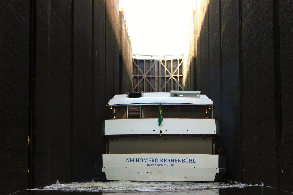 Barco de turismo branco dentro da câmara da eclusa, entre dois paredões altos de concreto