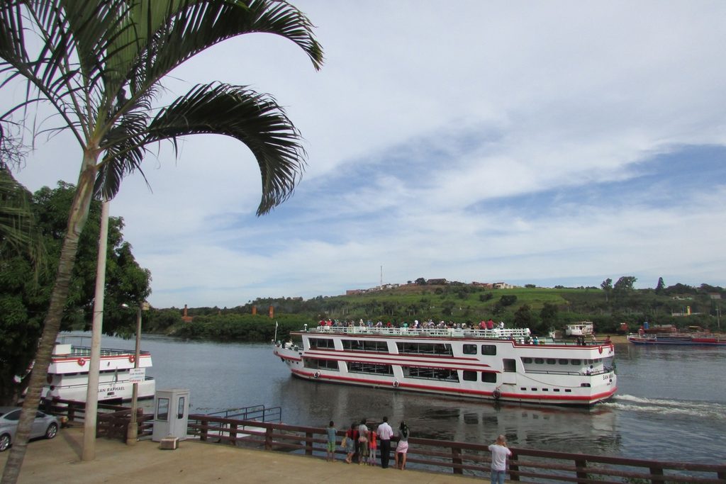 Barcos de turismo atracados no rio Tietê junto à orla de Barra Bonita, com palmeira e visitantes no deque