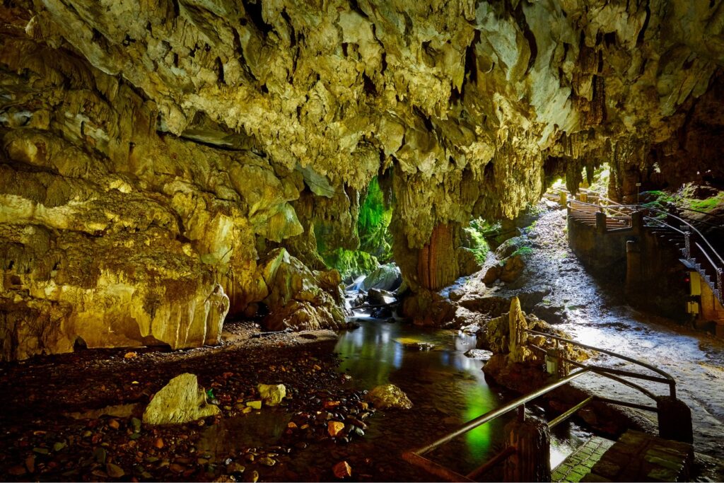 Interior da Caverna do Diabo com teto de rocha, rio subterrâneo iluminado e passarelas de madeira com corrimão