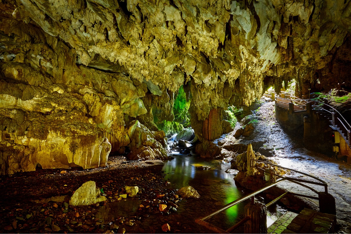 Interior da Caverna do Diabo com teto de rocha, rio subterrâneo iluminado e passarelas de madeira com corrimão