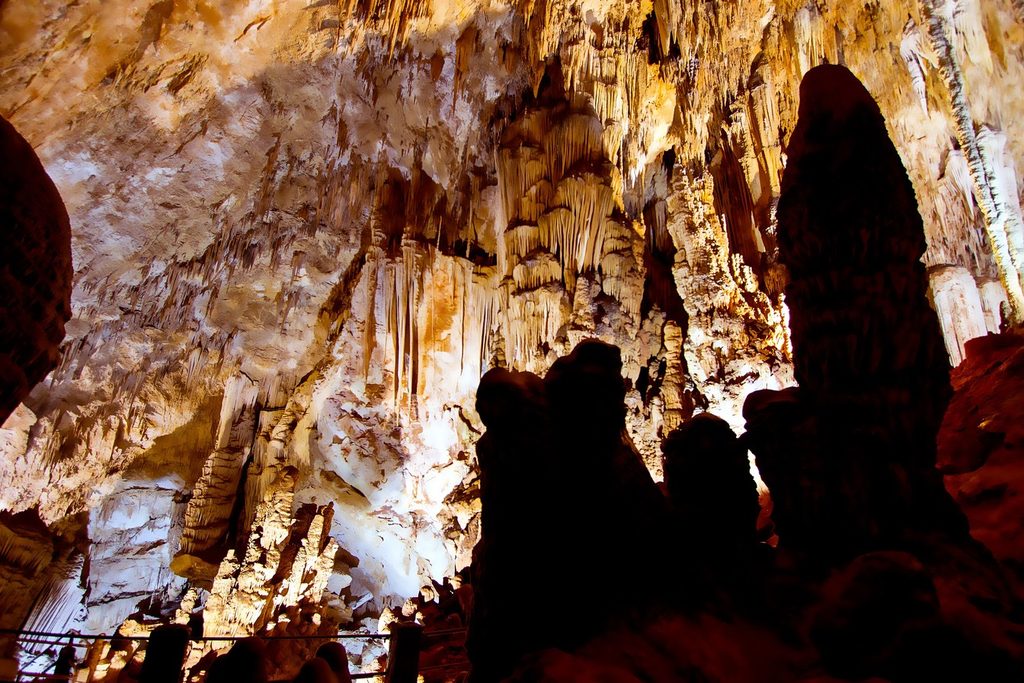Estalactites e colunas iluminadas em tons dourados no teto da Caverna do Diabo, com silhuetas de formações escuras