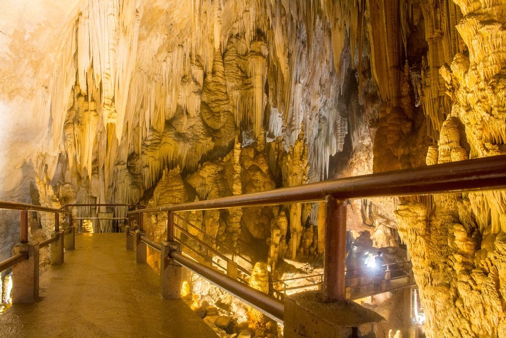 Passarela com corrimão atravessando um salão da Caverna do Diabo cheio de estalactites e colunas iluminadas