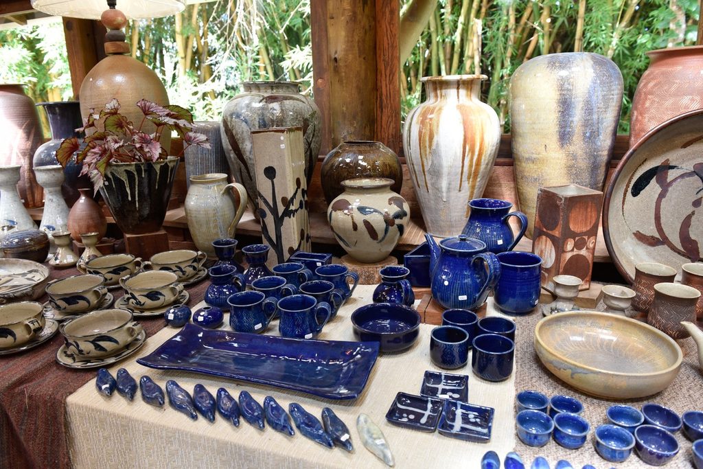 Mesa com vasos, xícaras e peças de cerâmica esmaltada em azul e tons de terra em um ateliê de Cunha