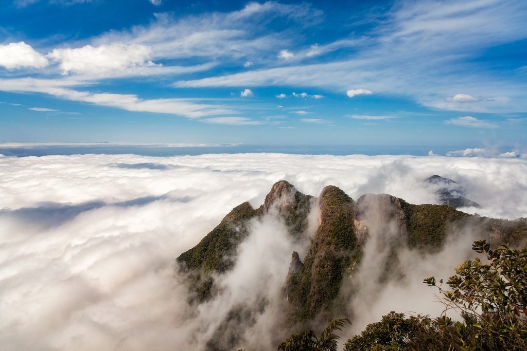Picos da região da Pedra da Macela emergindo de um mar de nuvens sob céu azul