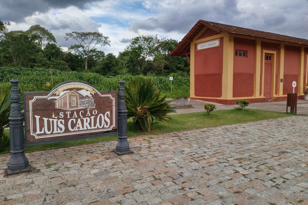 Placa e fachada da Estação Luís Carlos, em Guararema, cercada de vegetação