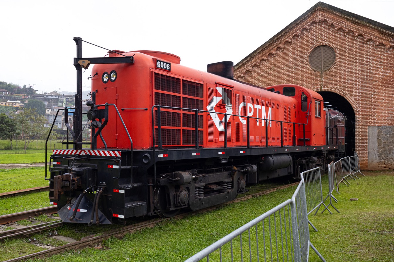 Locomotiva diesel vermelha ALCO RS-3 do Expresso Turístico da CPTM parada nos trilhos diante de um galpão de tijolos em Paranapiacaba