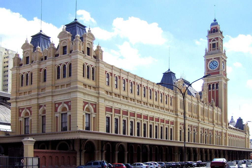 Fachada amarela e vermelha da Estação da Luz, ponto de partida do Expresso Turístico, com torre do relógio e janelas em arco