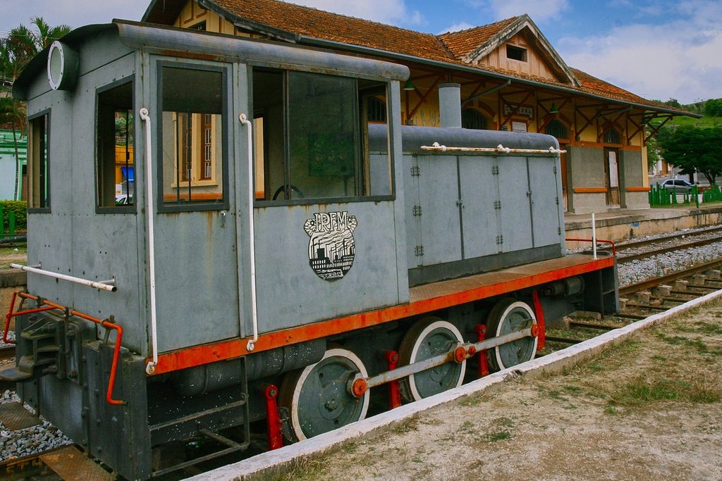 Pequena locomotiva cinza e vermelha exposta nos trilhos diante da estação de Sabaúna, em Mogi das Cruzes