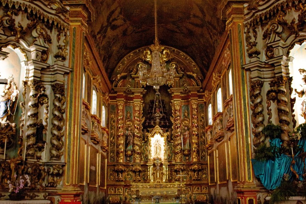 Interior da igreja com altar-mor e colunas cobertos de talha dourada em estilo barroco