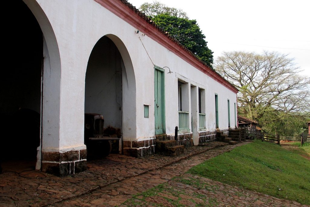 Construção térrea branca com arcos, portas verdes e chão de pedra, na Fazenda Mandaguahy, em Jaú
