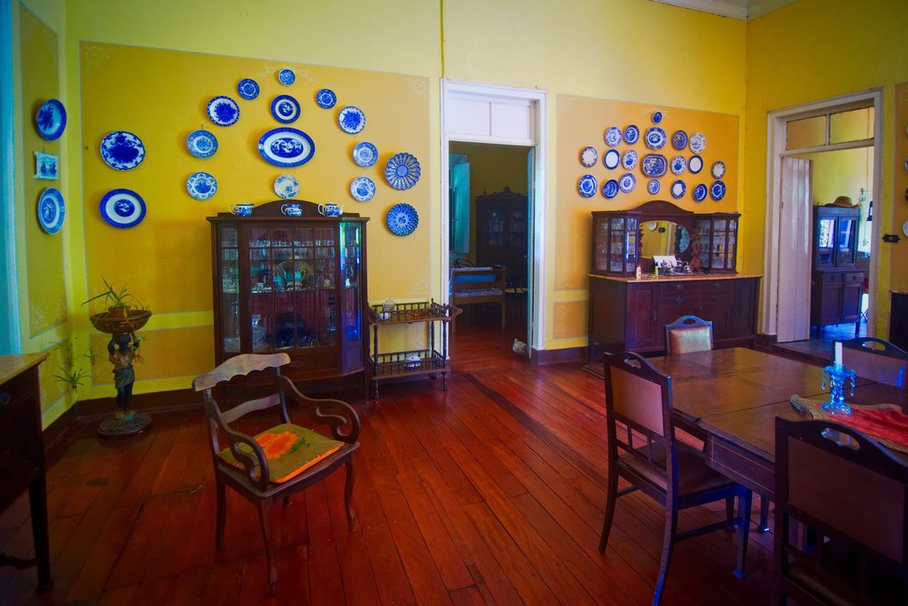 Sala de jantar com paredes amarelas decoradas com pratos azuis e brancos, cristaleiras de madeira e piso de tábuas