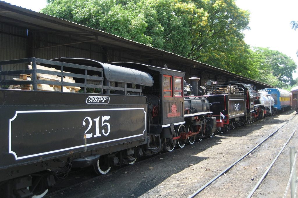 Locomotiva a vapor 215 da Maria Fumaça, preta com detalhes vermelhos, parada na plataforma coberta da Estação Anhumas, em Campinas