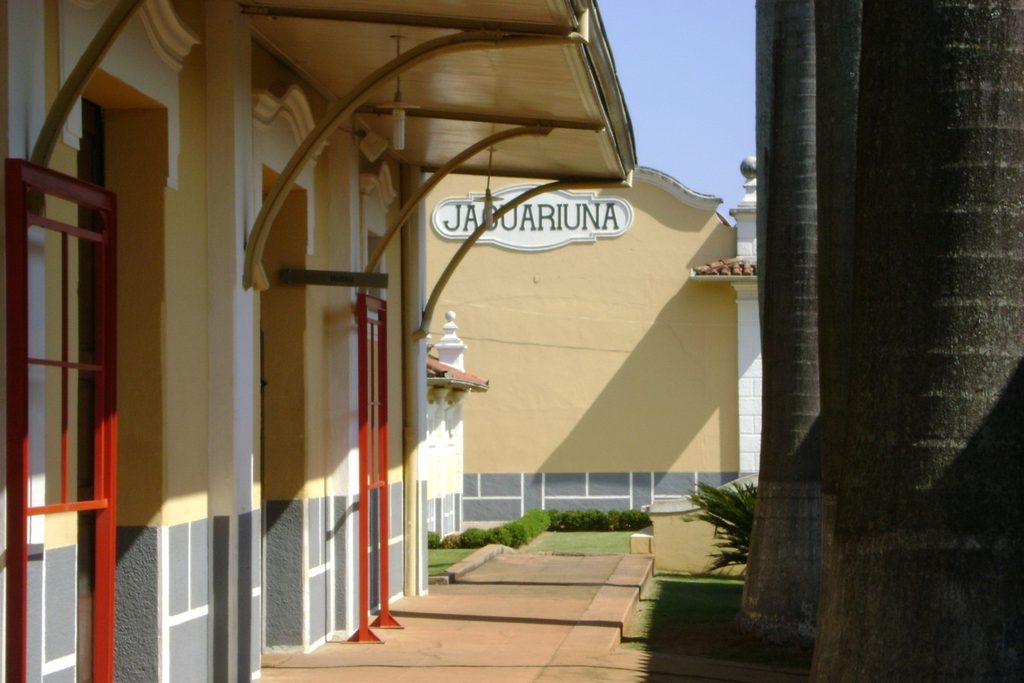 Plataforma coberta da Estação de Jaguariúna, com placa com o nome da cidade, colunas e portas vermelhas, ponto final da Maria Fumaça
