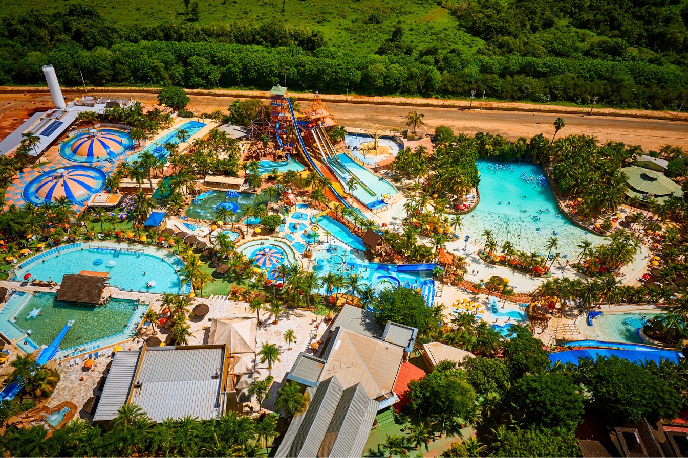 Vista aérea do Thermas dos Laranjais, em Olímpia, com piscinas azuis, escorregadores, piscina de ondas e palmeiras