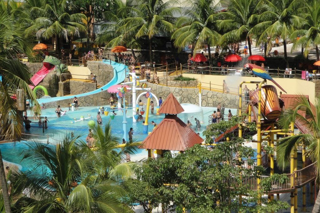 Área infantil de parque aquático com escorregadores coloridos, brinquedos e piscinas rasas entre palmeiras, no Thermas dos Laranjais