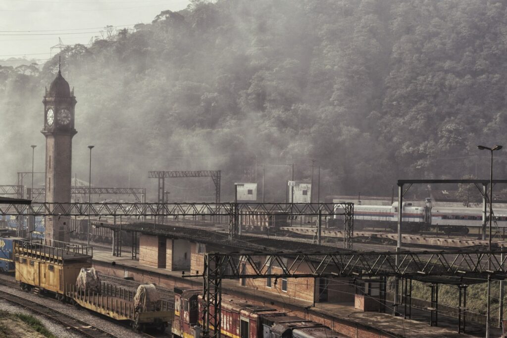 Torre do relógio de Paranapiacaba ao lado do pátio ferroviário, com trens e a serra coberta de neblina ao fundo