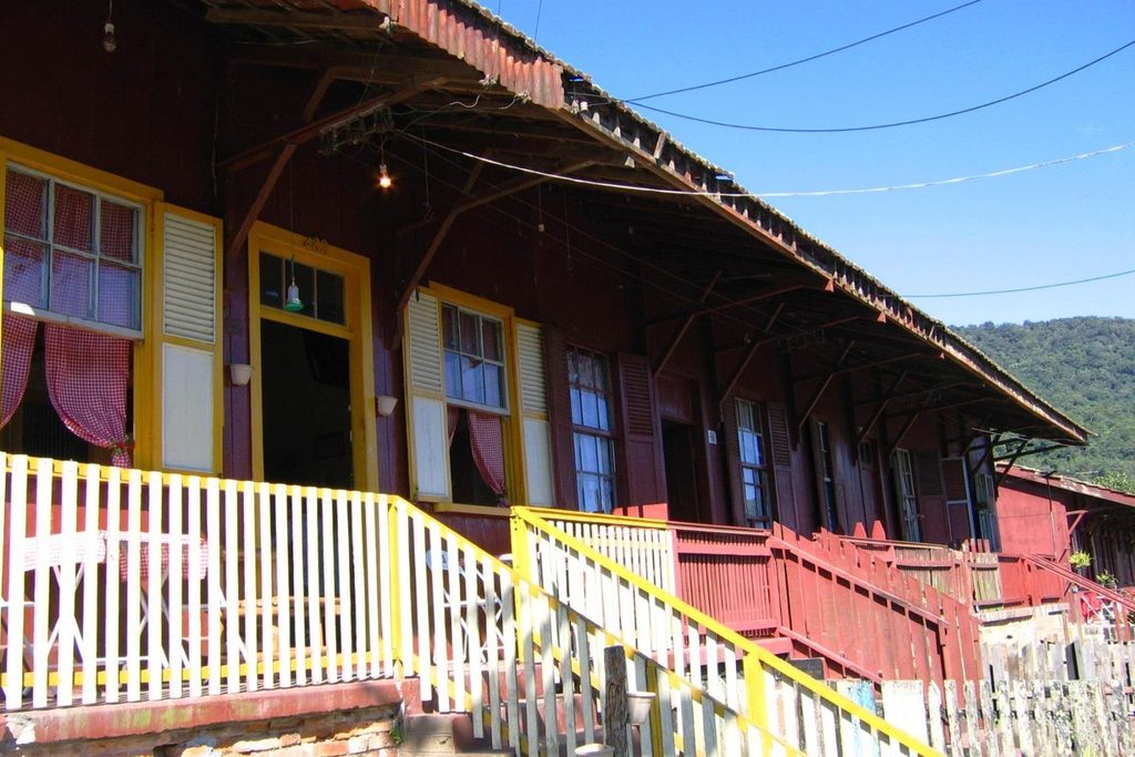 Casa de madeira vermelha com varanda e guarda-corpo branco e amarelo, com janelas de madeira, em Paranapiacaba