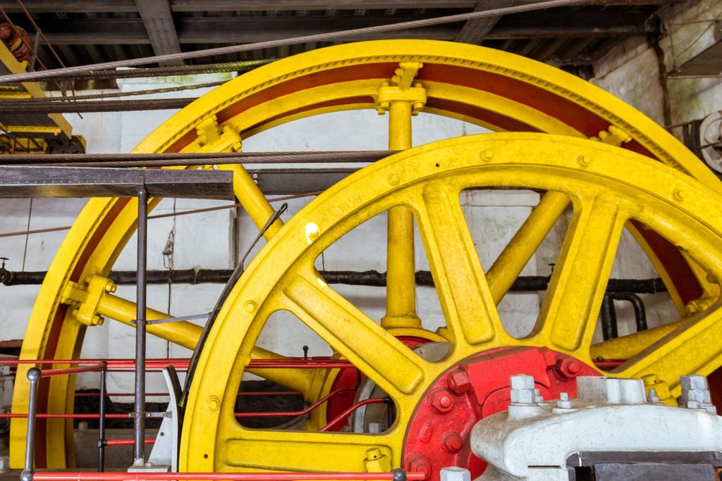 Grandes rodas de ferro amarelas e vermelhas da antiga máquina do sistema funicular, dentro de um galpão