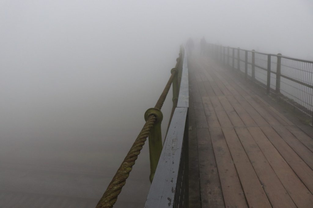 Passarela de madeira com corrimão sumindo na neblina densa, em Paranapiacaba