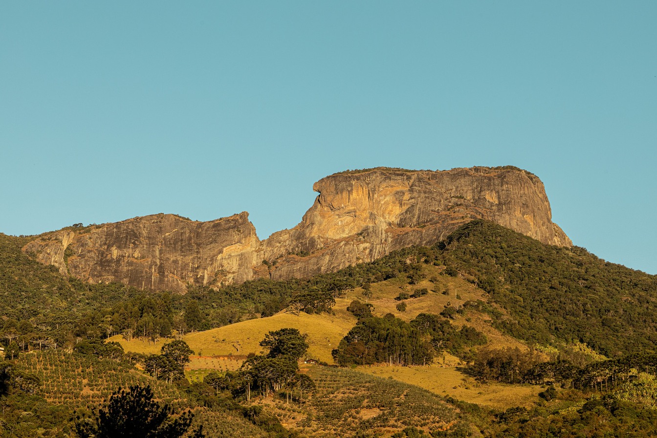 Complexo da Pedra do Baú, destino para o feriado de Finados, com paredões de pedra sobre morros de pasto e céu azul