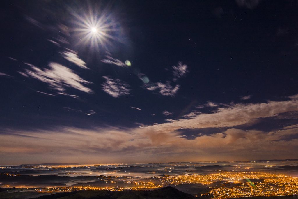 Céu noturno com lua e nuvens sobre as luzes das cidades no vale, vistas da Pedra Grande