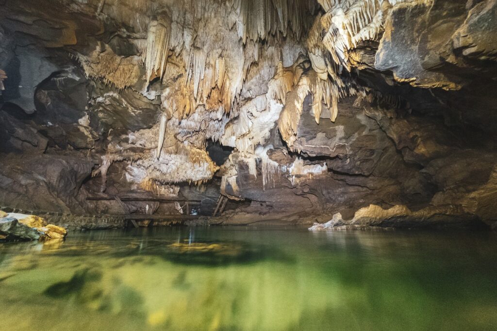Lago de água verde dentro da Caverna de Santana, com estalactites e paredes de pedra iluminadas ao fundo