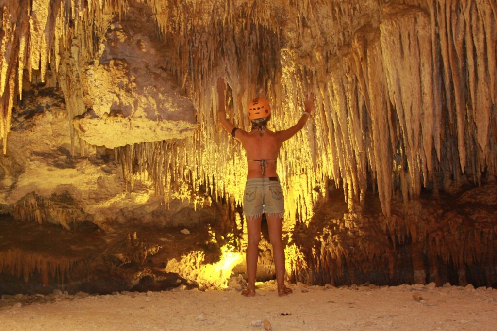 Visitante de capacete de costas diante de um teto cheio de estalactites douradas na Caverna de Santana