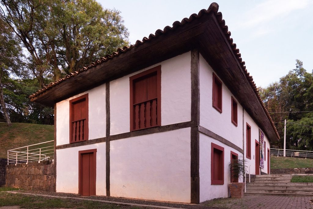 Casa térrea branca de estrutura de madeira aparente e janelas vermelhas, a Casa do Povoador