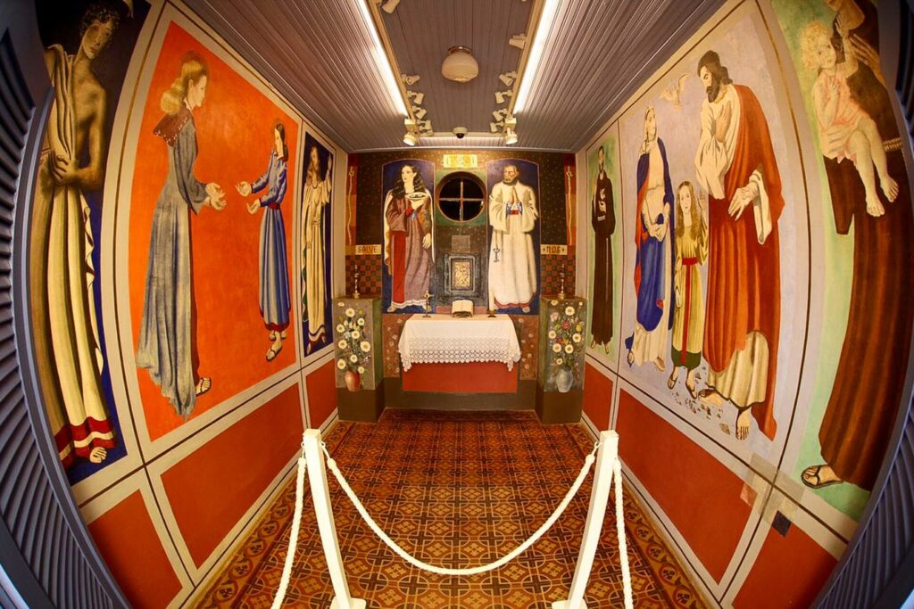 Interior da pequena Capela da Nonna, com paredes cobertas de murais coloridos de santos pintados por Portinari e altar ao fundo