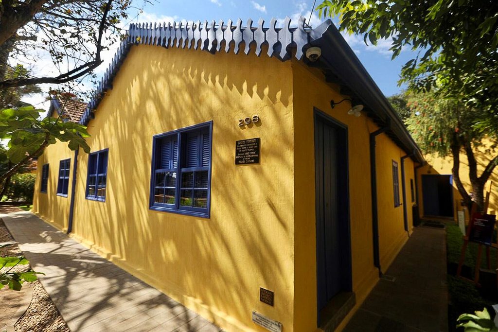 Casa térrea amarela de janelas azuis, a Casa de Portinari, em Brodowski, com calçada e árvores