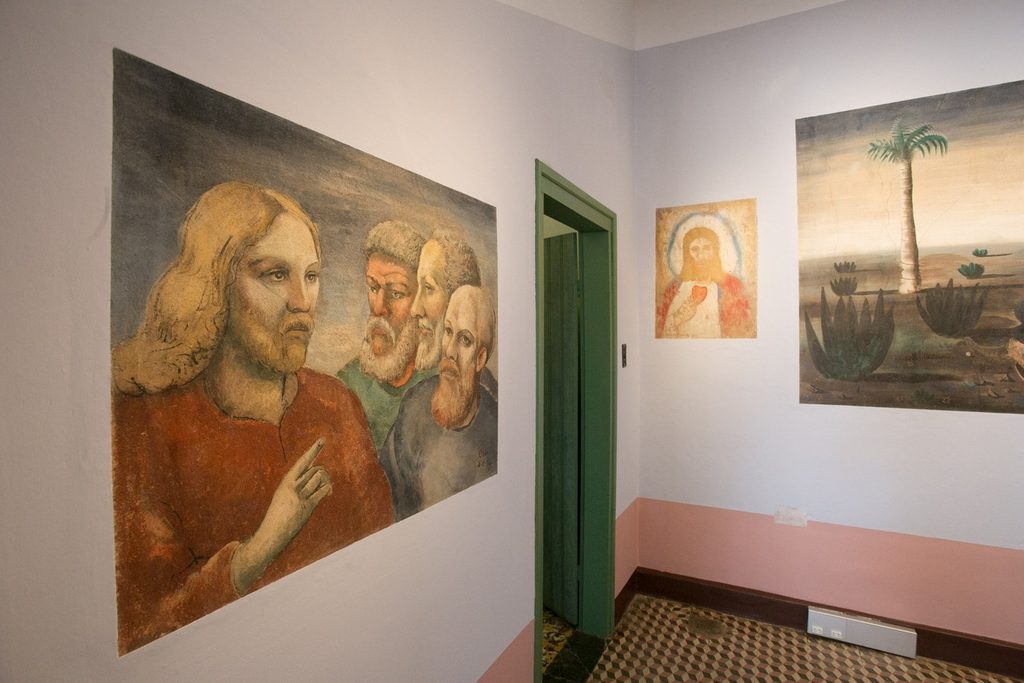 Pinturas murais de Portinari nas paredes brancas de um cômodo da casa, com rosto de Jesus e apóstolos