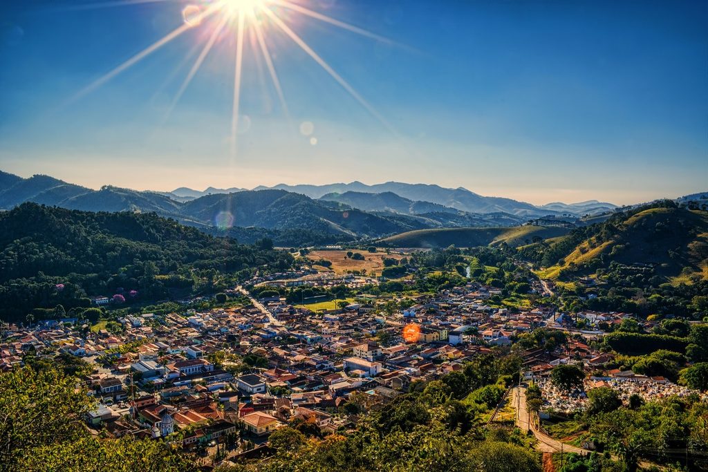 Vista do alto da cidade de São Bento do Sapucaí, com casas no vale cercado de montanhas e sol forte no céu
