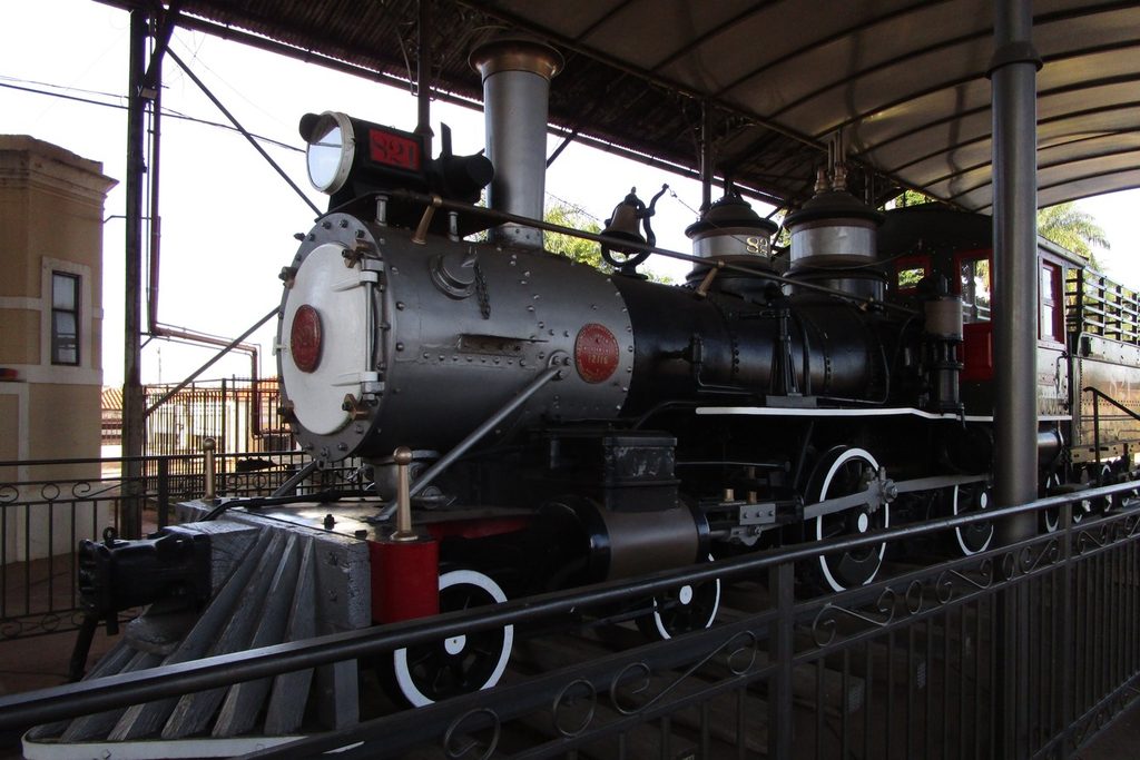 Locomotiva a vapor preta e vermelha exposta sob cobertura na plataforma da estação de São Carlos