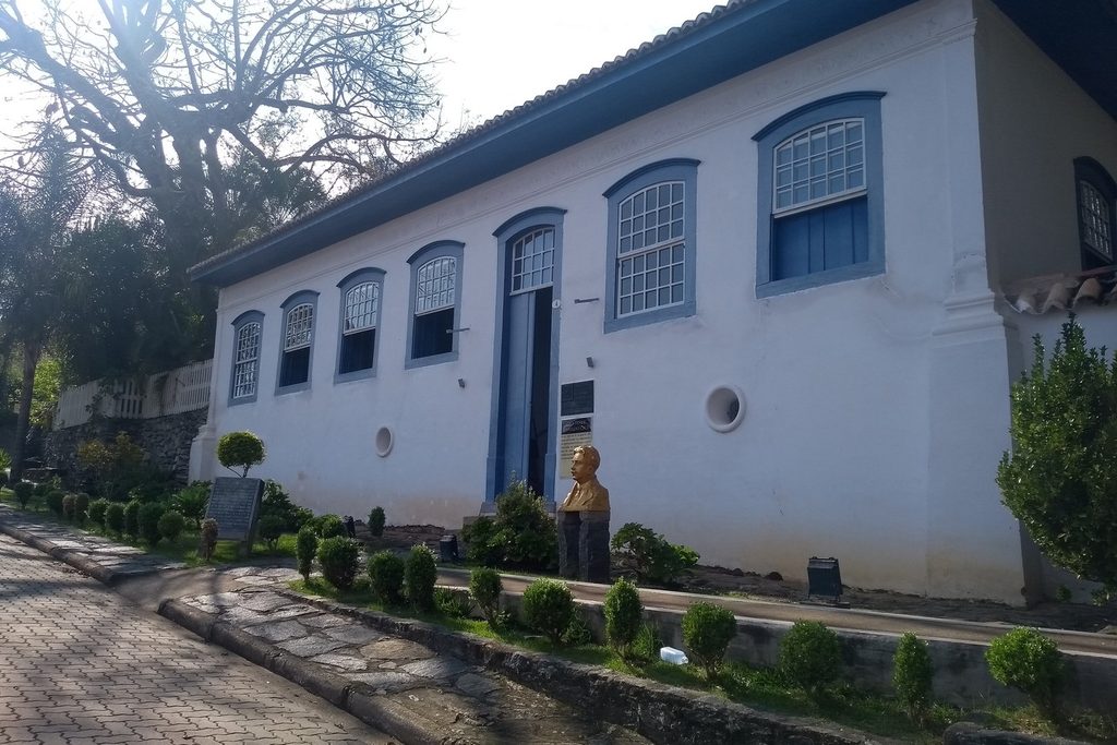 Casarão térreo branco de janelas azuis com busto na frente, a casa onde nasceu Oswaldo Cruz, em São Luiz do Paraitinga