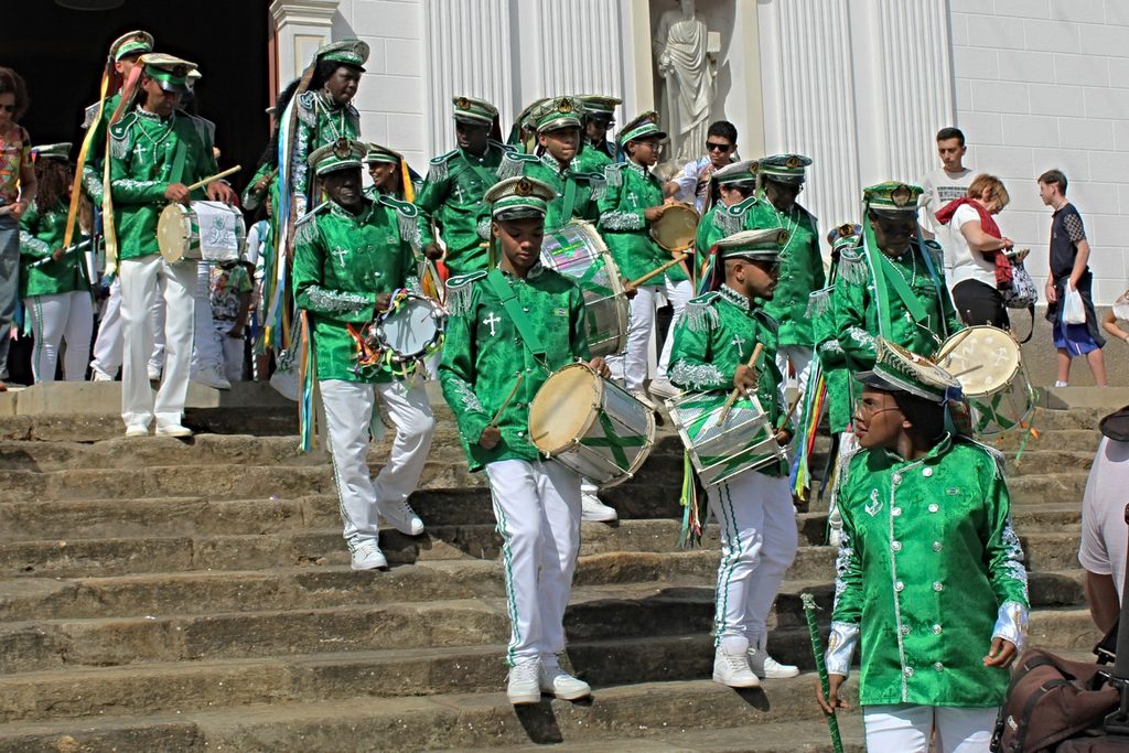 Grupo de congada com roupas verdes e brancas tocando tambores na escadaria da igreja