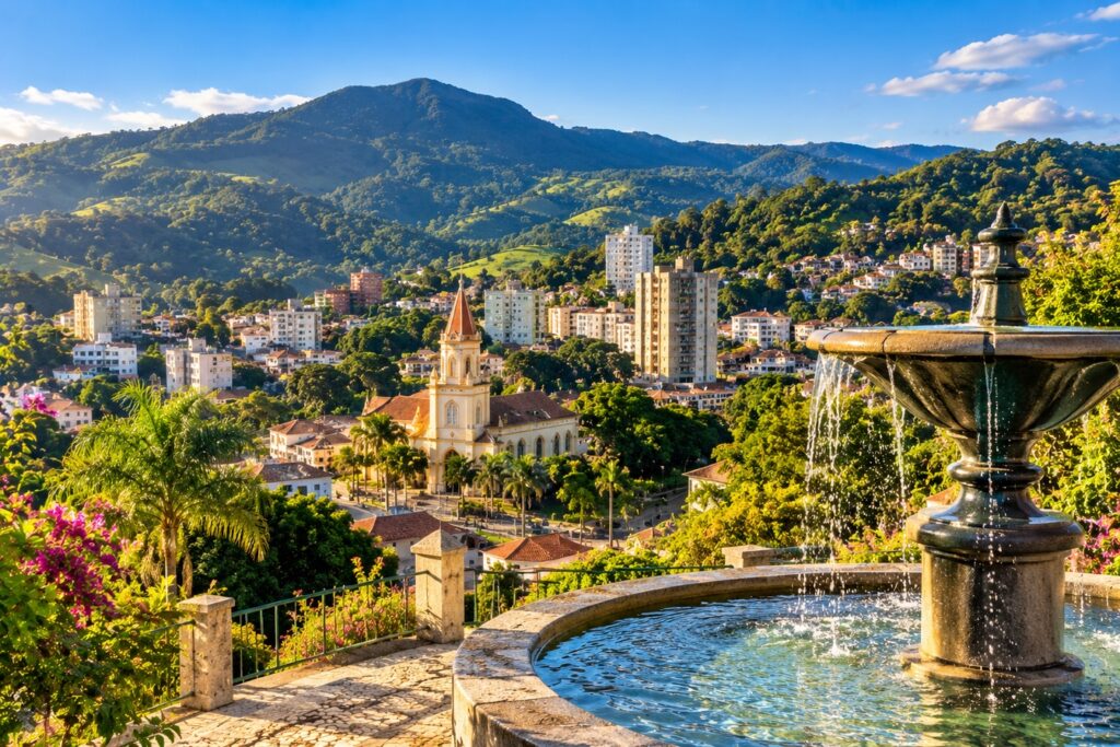 Vista ilustrada de Serra Negra com a cidade entre montanhas verdes, uma igreja ao centro e um chafariz em primeiro plano