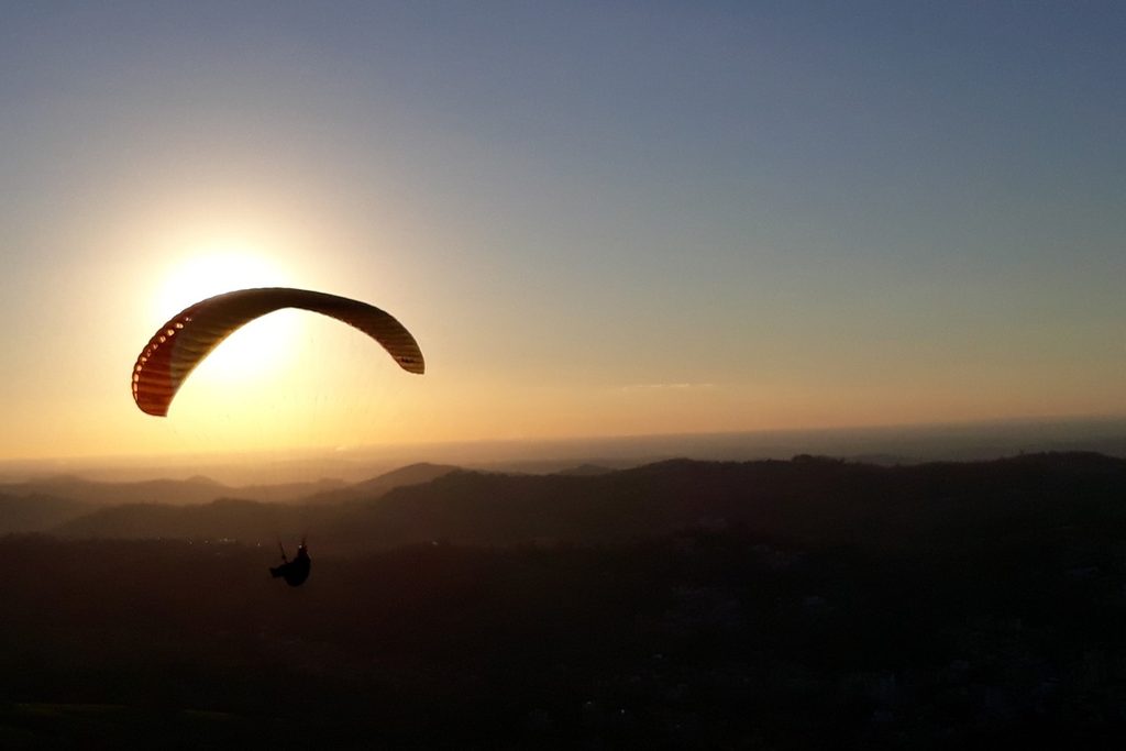 Parapente em silhueta contra o pôr do sol, sobre as serras de Serra Negra