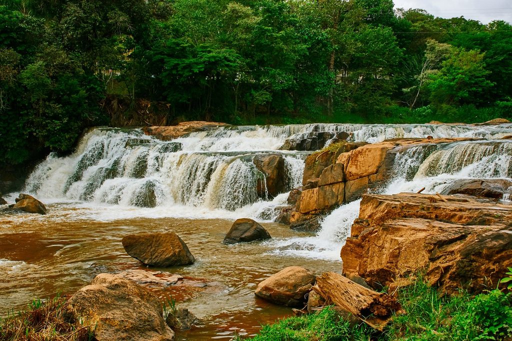 Cachoeira larga descendo em degraus sobre pedras alaranjadas, cercada de mata