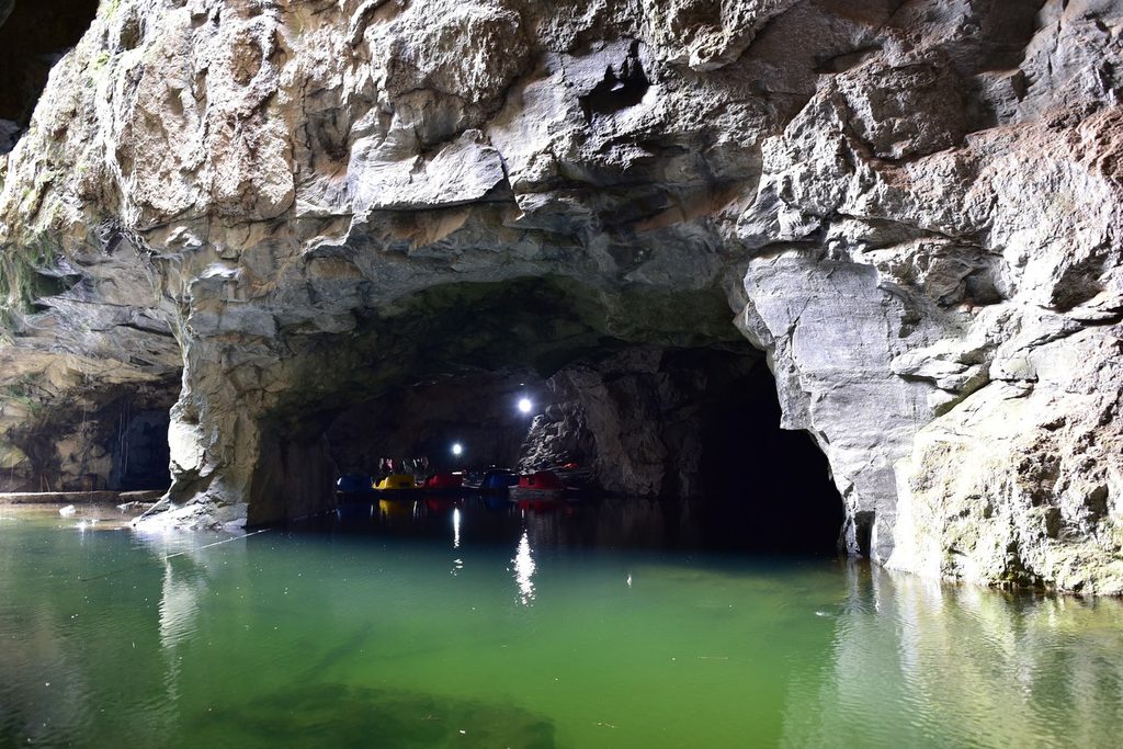 Lago de água verde e cristalina dentro da Gruta do Anjo, cercado por paredões de rocha e com visitantes em pedalinhos ao fundo