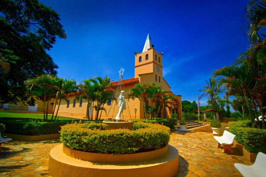 Igreja amarela de torre com relógio e praça com fonte, jardim circular e imagem branca de Nossa Senhora, o Santuário de Fátima de Tatuí
