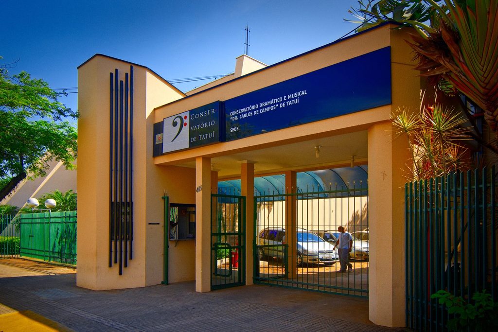Entrada da sede do Conservatório Dramático e Musical Dr. Carlos de Campos, com fachada bege, letreiro azul e portão verde