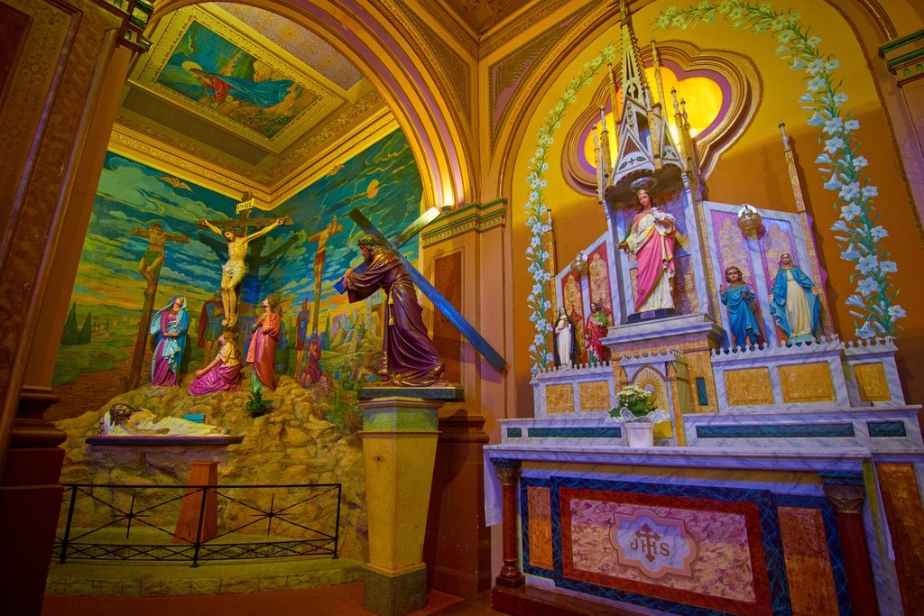 Interior colorido da igreja com altar de imagens de santos e pintura do Calvário na parede lateral