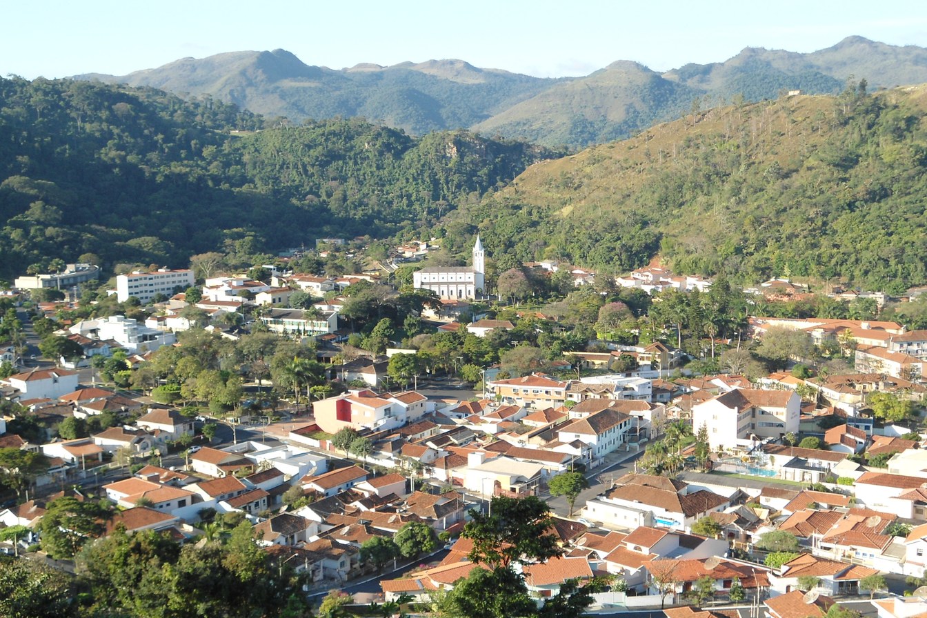 Vista do alto de Águas da Prata, com casas de telhado vermelho, a igreja branca no centro e montanhas cobertas de mata ao redor