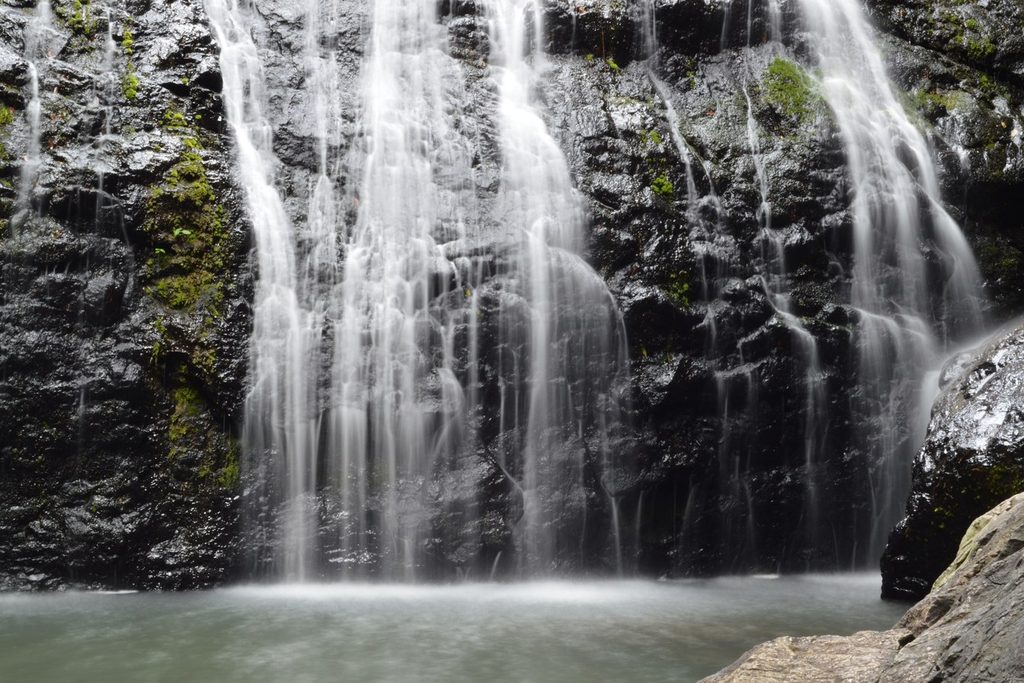 Vários fios de água descendo por um paredão de pedra escura até um poço largo, na última queda da Sete Quedas