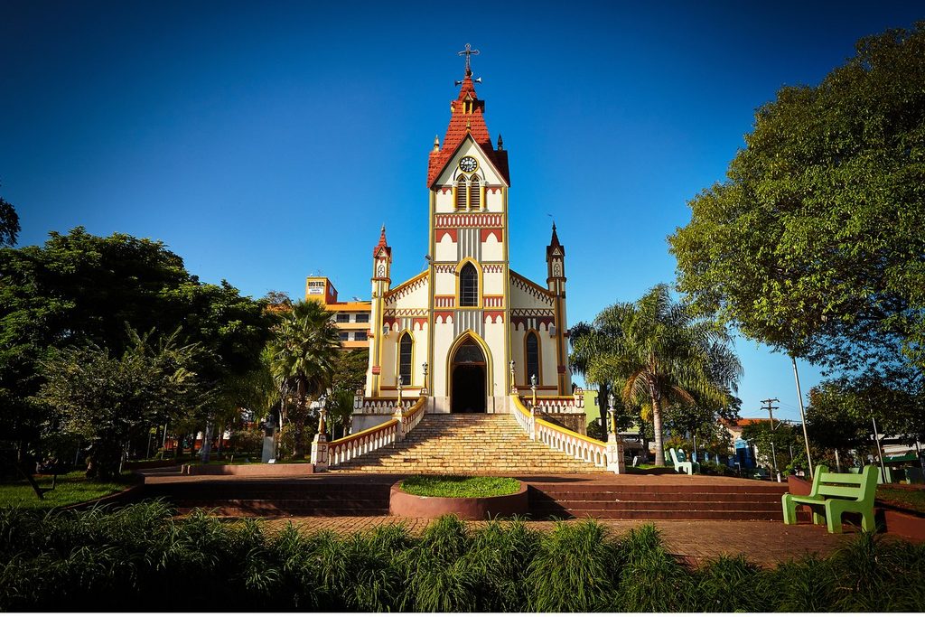 Igreja Matriz de Santa Bárbara, branca com detalhes vermelhos e torre pontuda, no alto de uma escadaria