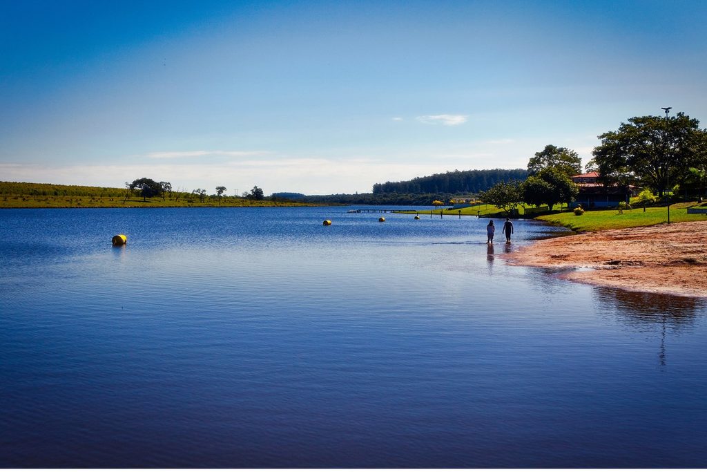 Prainha de areia na beira do lago azul do Parque dos Lagos, em Águas de Santa Bárbara, num dia de céu limpo