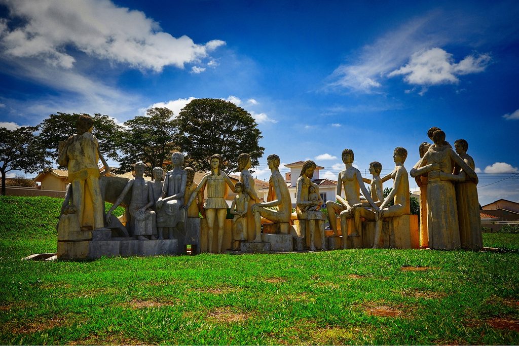 Grupo de esculturas de Bassano Vaccarini com figuras humanas sentadas lado a lado num gramado, em Altinópolis