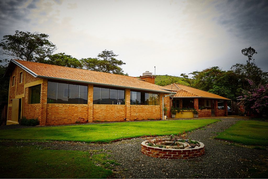 Construção de tijolos com telhado de telhas e grandes janelas de vidro da Vinícola Terrassos, com gramado e árvores em volta